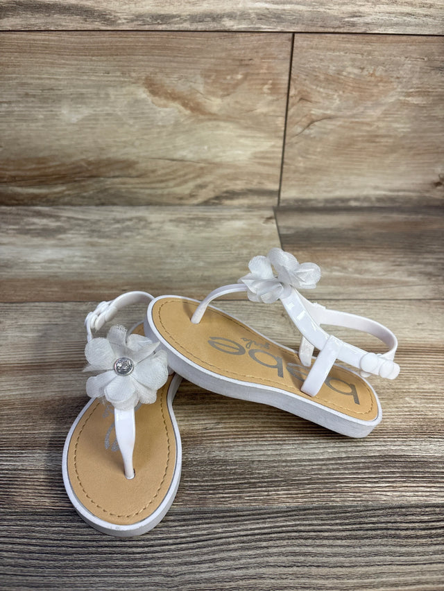 Front-angle of Bebe chiffon flower sandal showcasing sheer white chiffon flower with rhinestone center on wood background