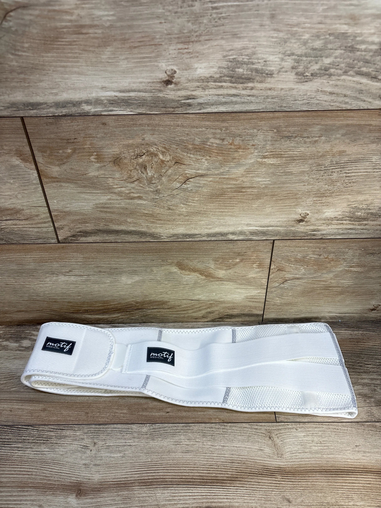White Motif Medical postpartum belly band on wood floor, maternity support belt