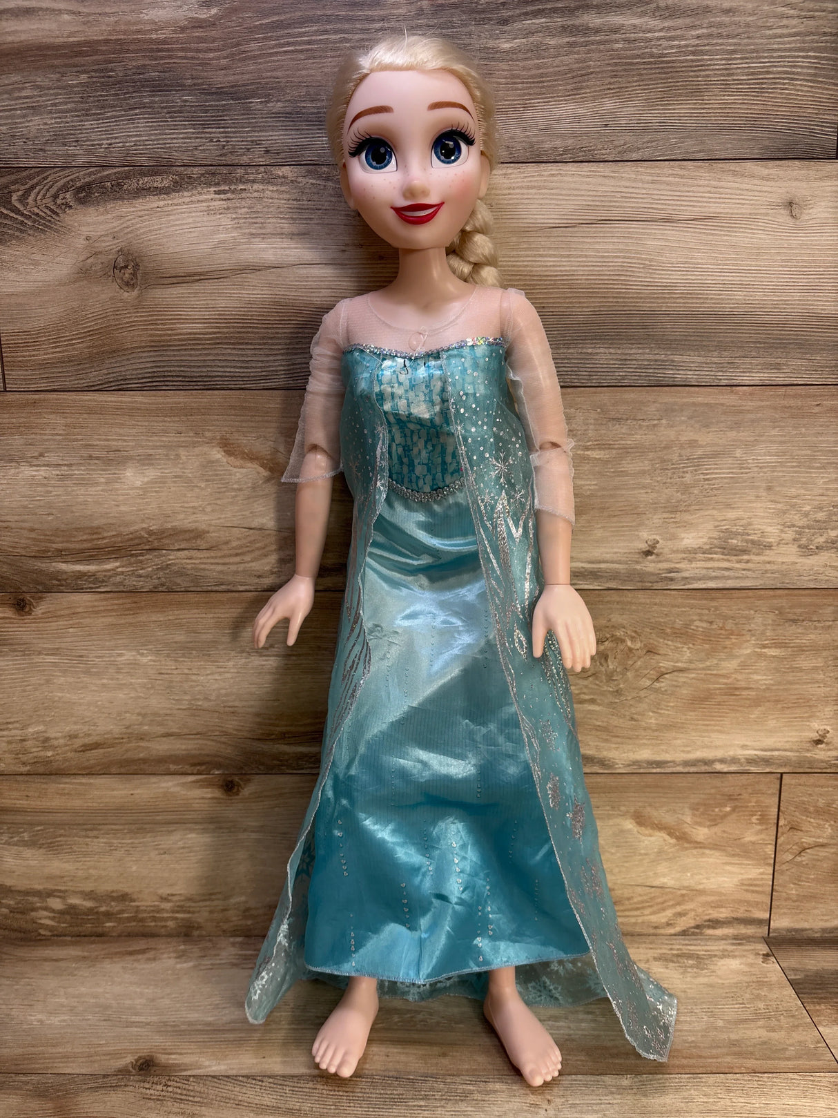 Front view of 32-inch Elsa doll in blue glitter gown with braided blonde hair, painted face, bare feet on wood background