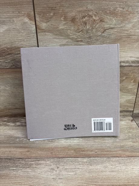 Back view of Growing Up memory book showcasing gray fabric cover and Korie Herold logo on a wood surface