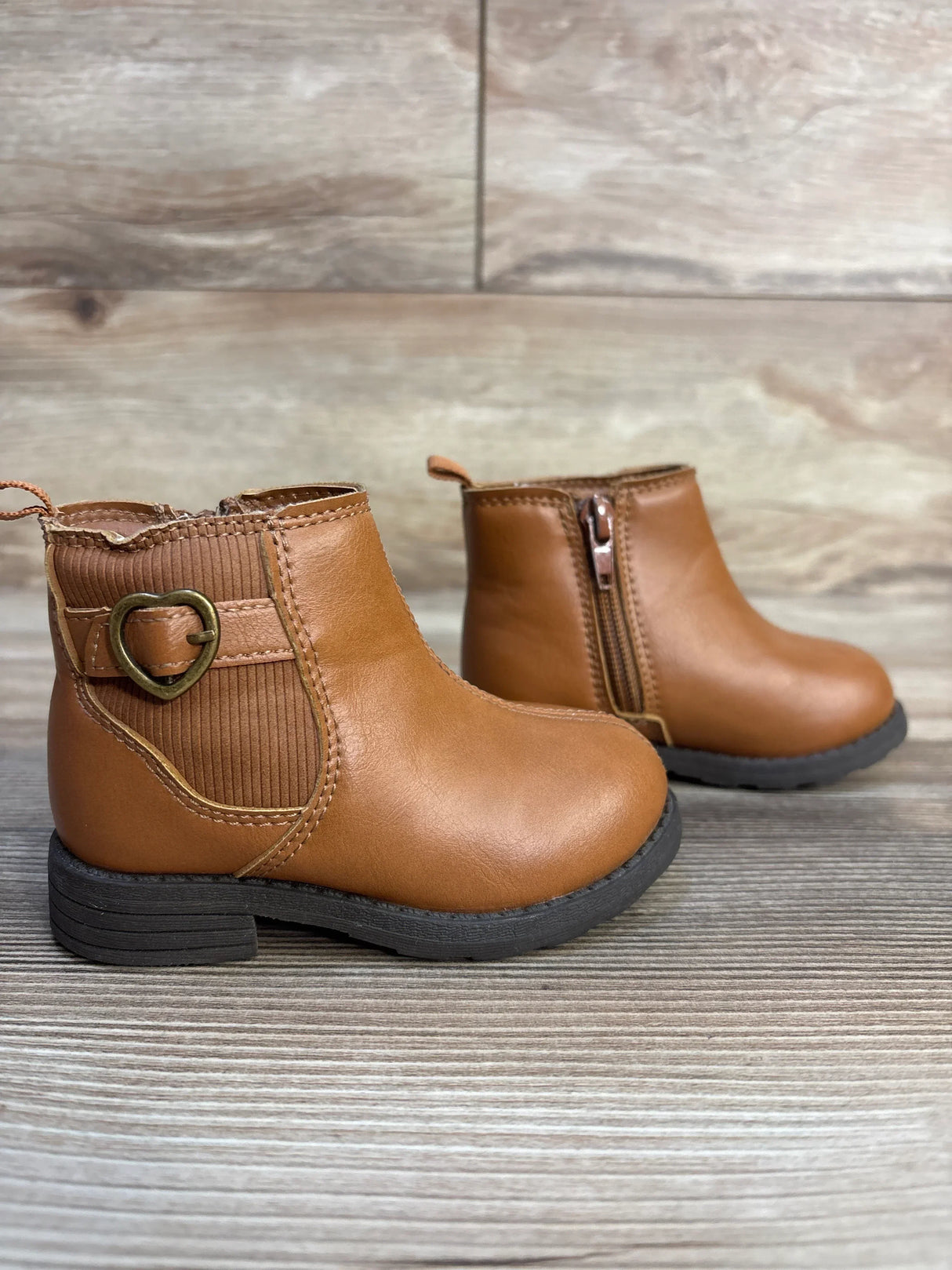 Brown toddler ankle boots with side zipper and heart buckle, on wood floor background