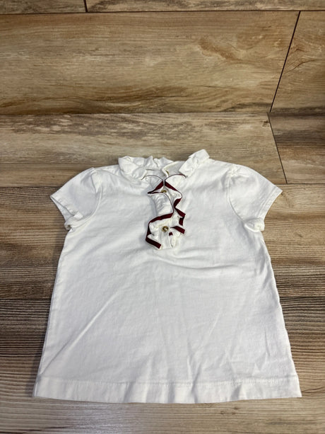White Janie & Jack ruffle henley top for toddlers with burgundy trim on a wooden background.
