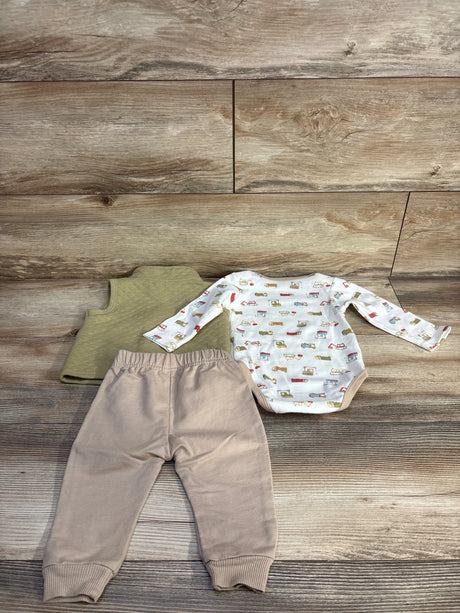Flat lay of Chick Pea 3-piece baby set showing truck-print bodysuit, olive vest, and tan pants on wood