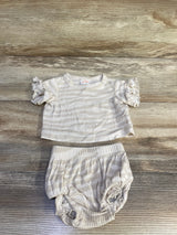 Top-down view of ivory newborn ribbed two-piece: short-sleeve ruffle shirt and bloomers showing ribbed texture on wood background