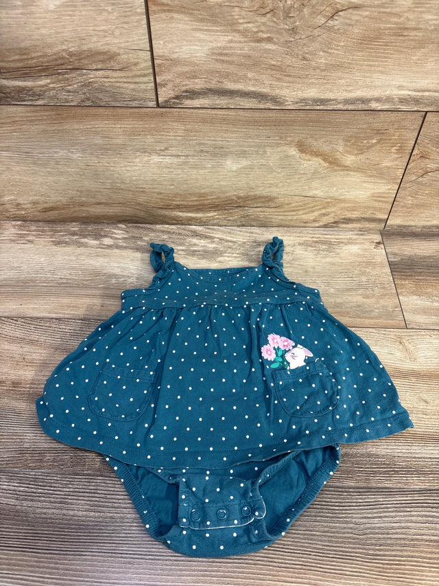Front view of teal polka dot baby bodysuit dress with ruffle straps, bunny-printed pocket and crotch snaps on wood background