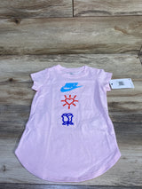 Front flat-lay of pink Nike toddler shirt with blue NIKE logo, red heart-sun and blue rose graphics on wood background