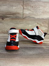 Toddler Jordan 11 sneakers in black, white, and red with velcro straps, displayed on wood floor
