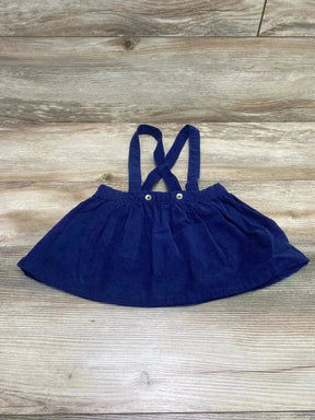 Flat lay of navy corduroy toddler suspender skirt with crossed adjustable straps and button details on a wood background
