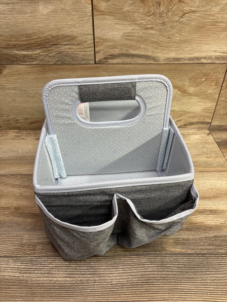 Front view of grey Munchkin portable diaper caddy showcasing two exterior pockets and open storage area on wood floor