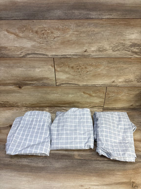 Overhead view of three folded fitted bassinet sheets showcasing light gray fabric with white windowpane grid pattern on wood background