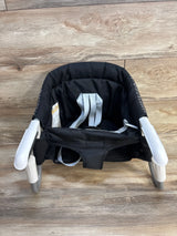 Black portable clip-on high chair with safety straps for babies, shown on wood floor