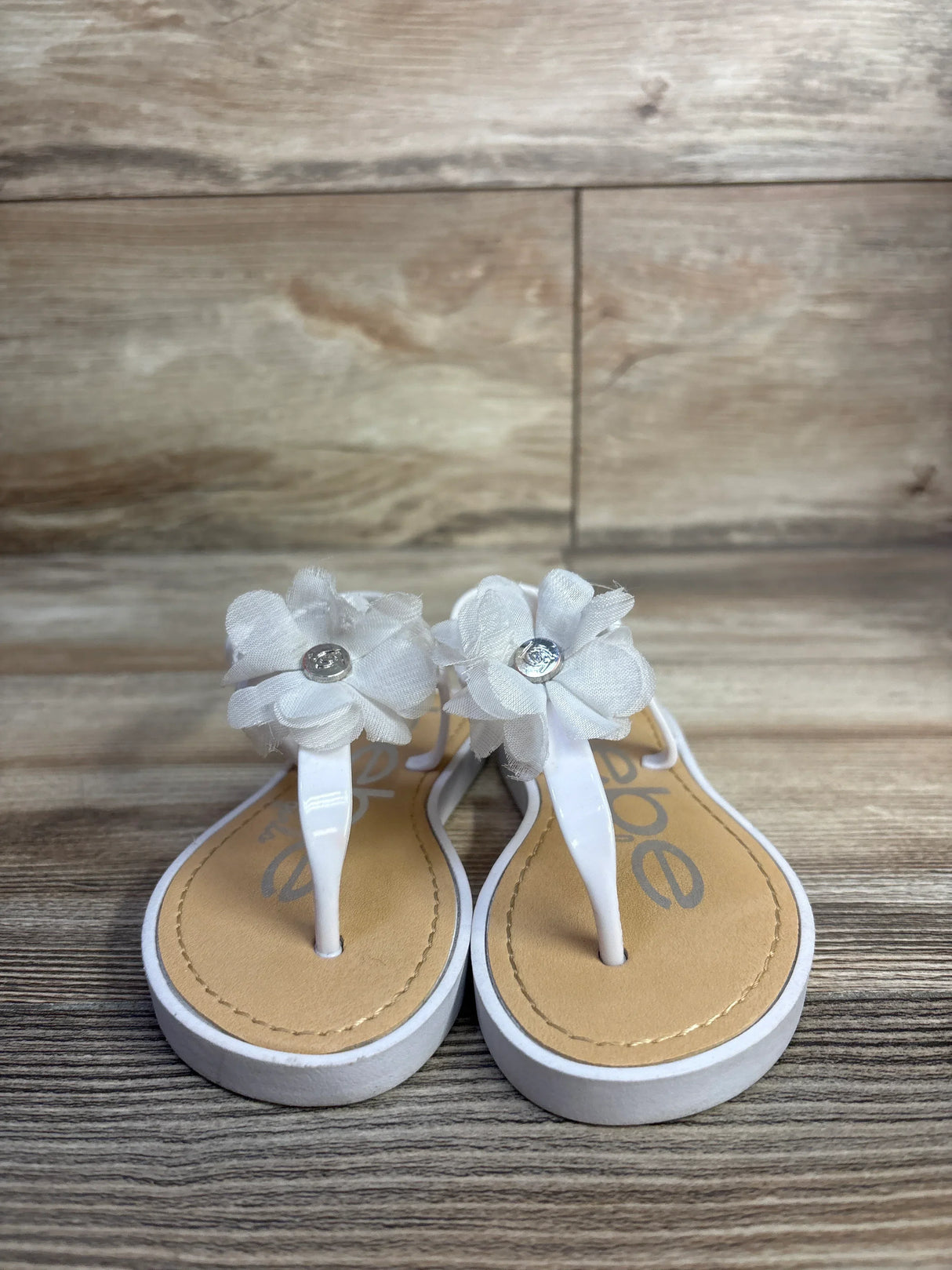 Front view of Bebe white chiffon flower sandals showing fabric flowers with rhinestone centers on wood background