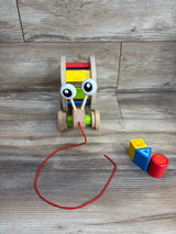 Wooden pull-along toy with large eyes and colorful rolling drum beside three colorful stacking blocks on wood surface