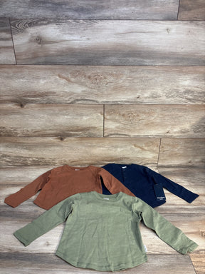 Flat lay of Gerber Kids 3-pack long-sleeve henley shirts size 3T in green, rust, and navy showing henley placket on wood floor