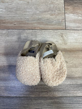 Top view of Child of Mine beige baby clogs showing plush curly texture and elastic heel straps on light wood floor