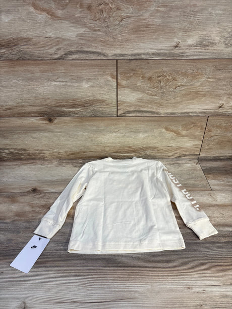 Back view of Nike 2T long-sleeve toddler shirt in coconut cream showing sleeve 'Just Do It' text on wood floor