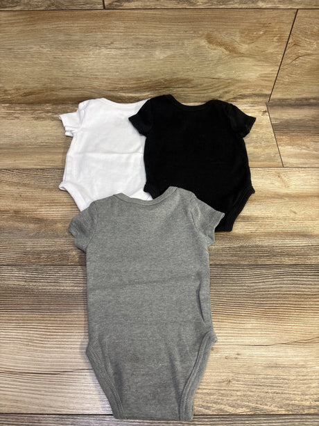 Top view of Nike three-pack baby bodysuits in white, black, and gray, size 3 months, on a wood floor