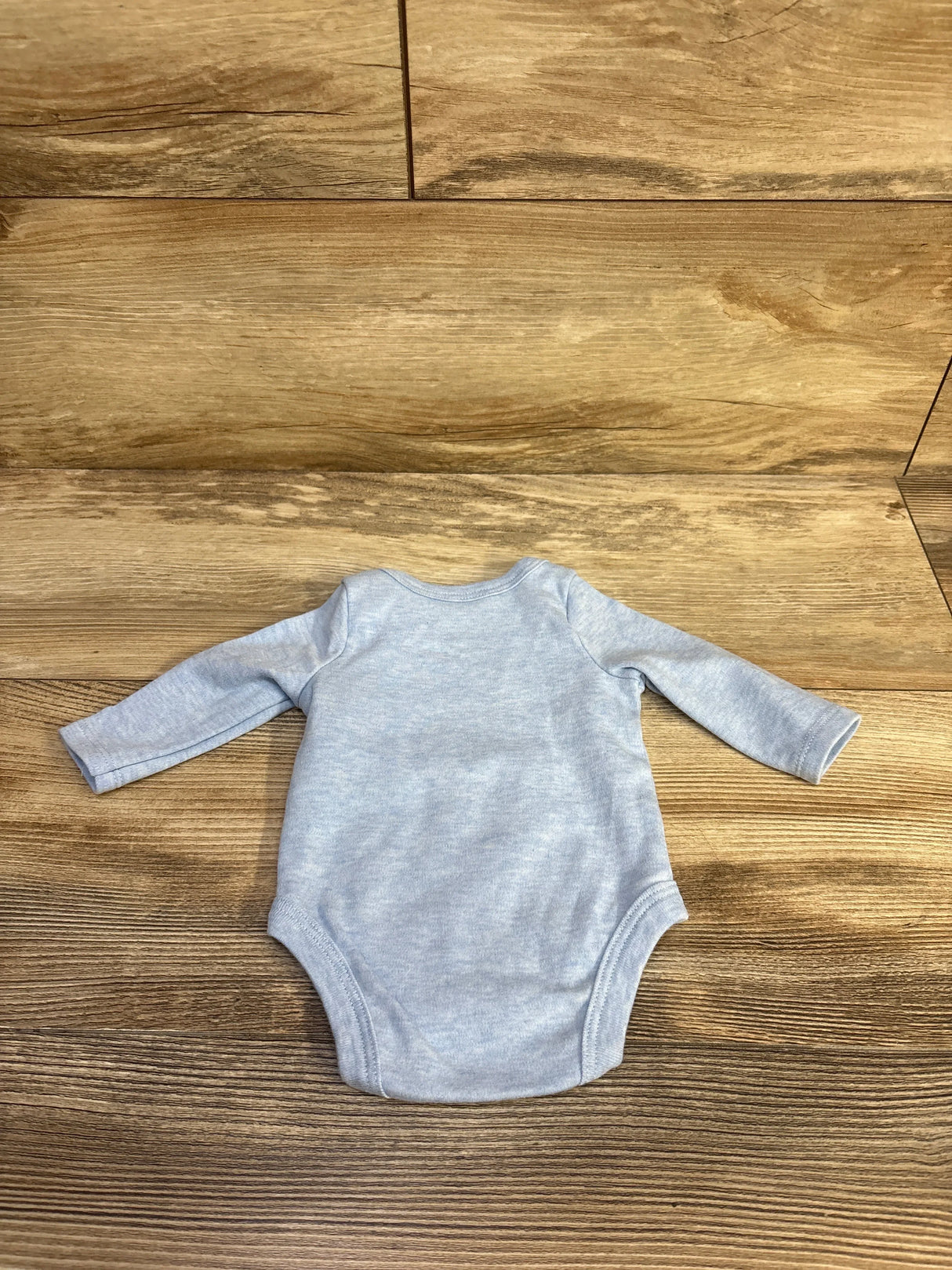 Flat lay of Sterling Baby newborn blue long-sleeve bodysuit showing back and full sleeves on wood background