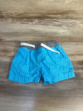 Flat lay of Carter's blue shorts 3-6M showing grey elastic waist with white drawstring and pockets on wood background