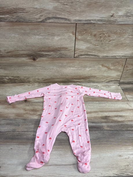 Flat lay of a pink heart-print baby sleeper showcasing long sleeves and footed legs on a wood-look background