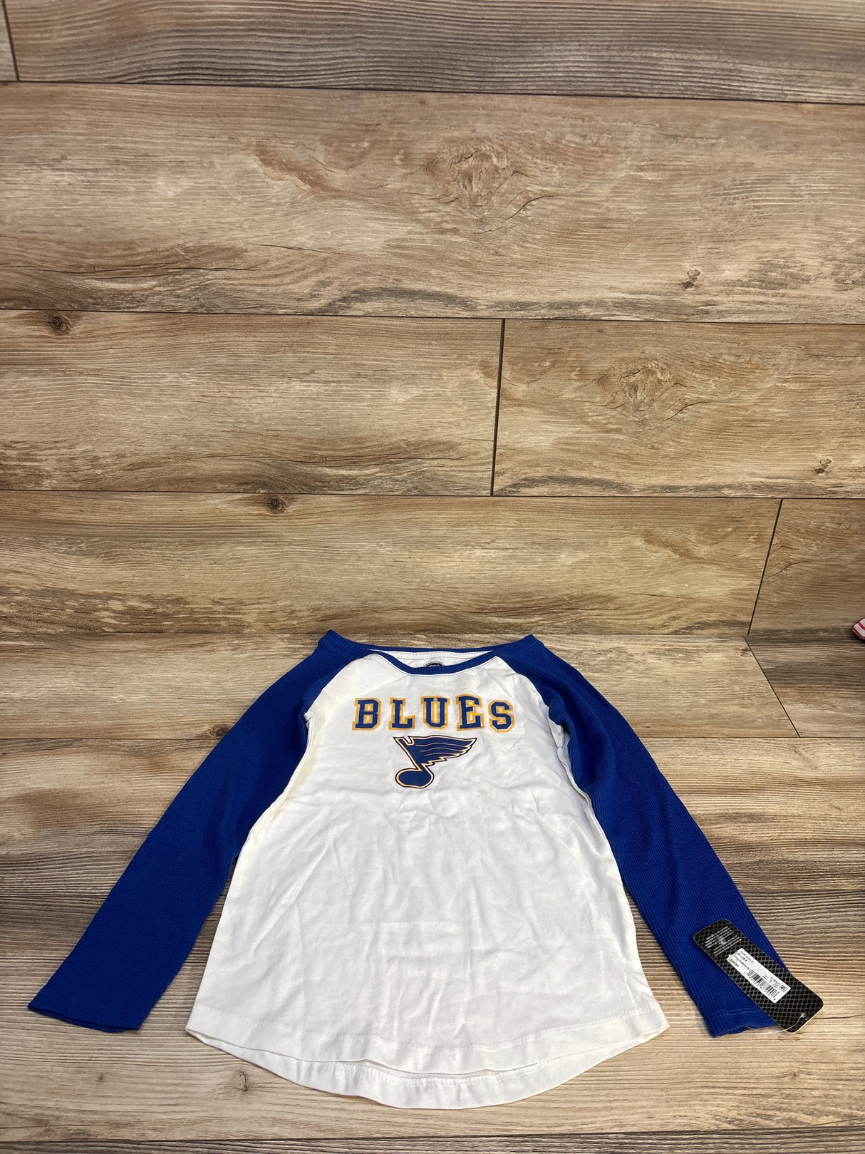 Blue and white kids' long sleeve raglan shirt with 'Blues' hockey logo on wooden floor