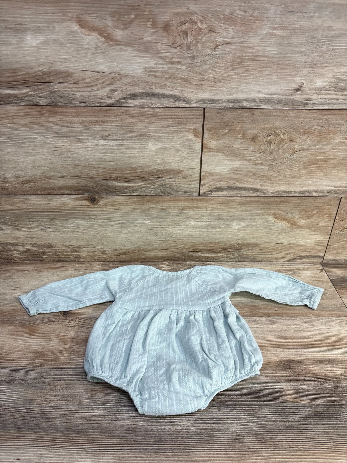 Front view of RZ by Rachel Zoe pale green romper with long sleeves and gathered waist, laid flat on wood, size 6–9m
