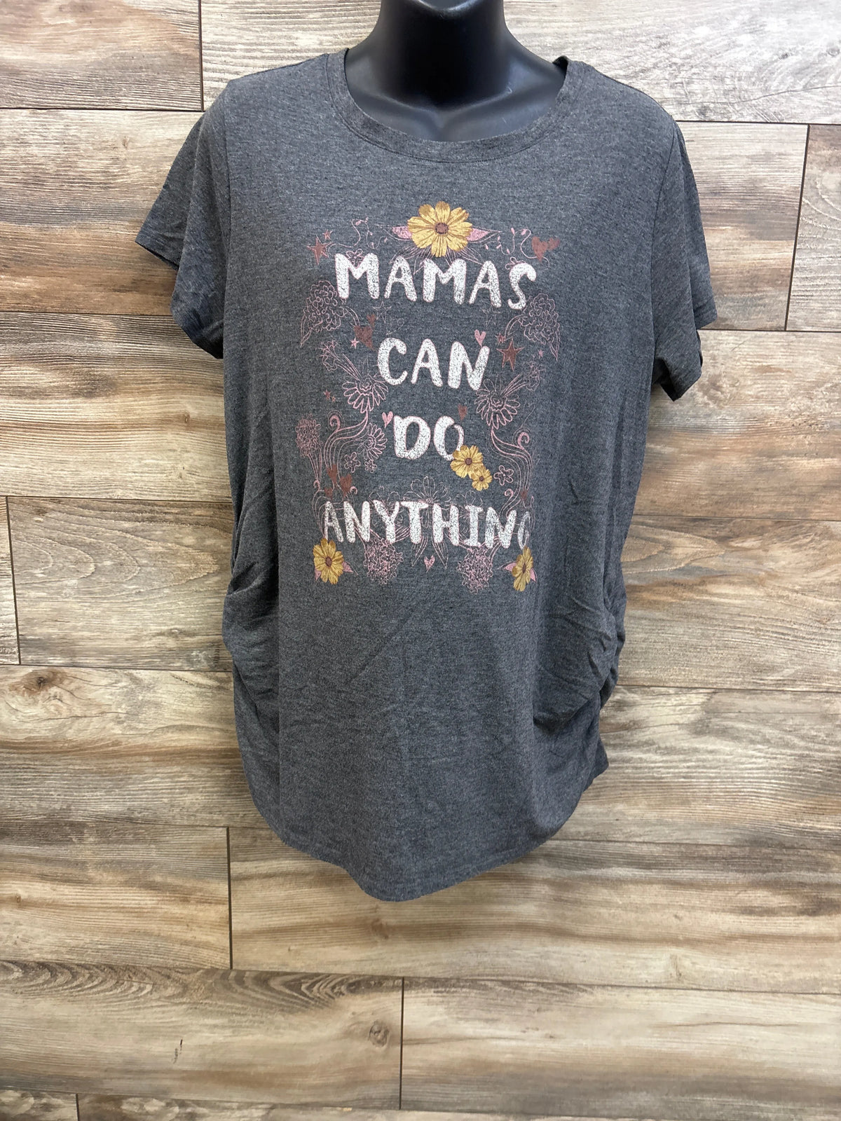 Front view of a grey maternity shirt showcasing floral MAMAS CAN DO ANYTHING graphic on wood backdrop
