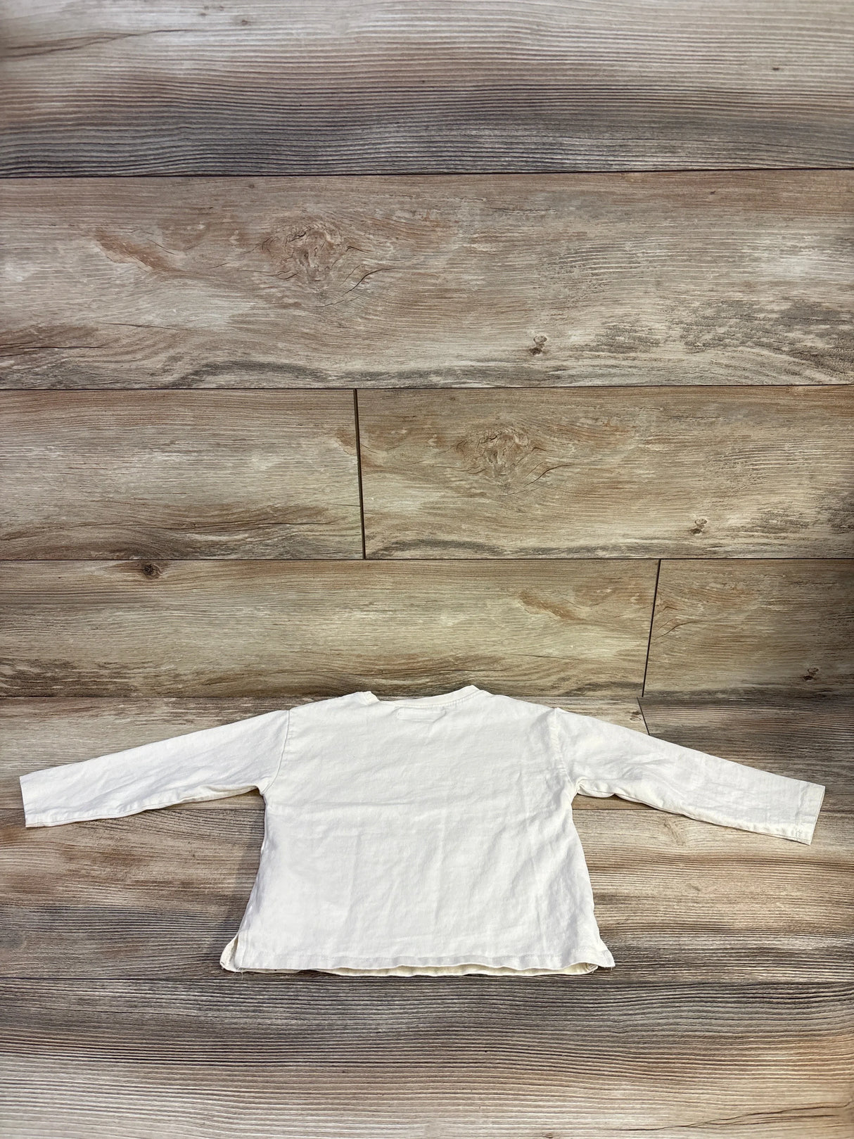 Back view of Zara ivory long sleeve toddler shirt showcasing long sleeves and raw hem on wood floor background