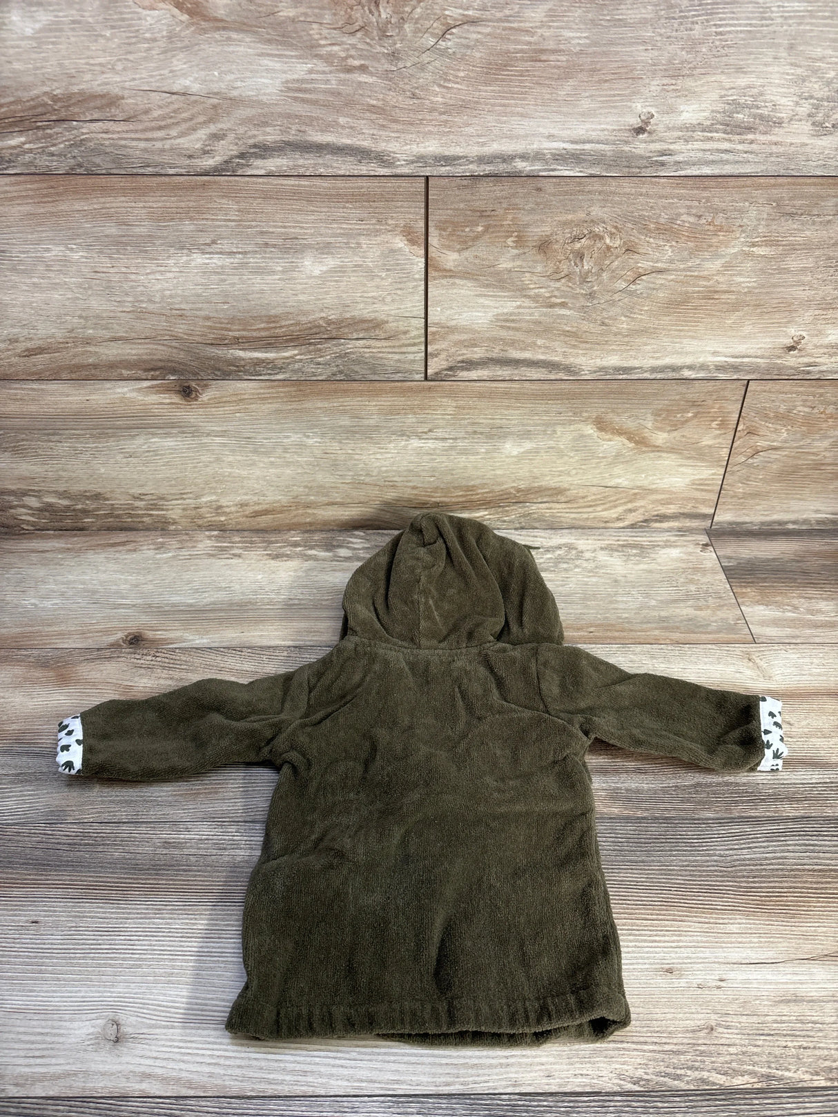 Flat-lay back view of Baby Essentials dinosaur hooded bath robe showcasing soft green terry fabric and dinosaur-print cuff lining on wood background