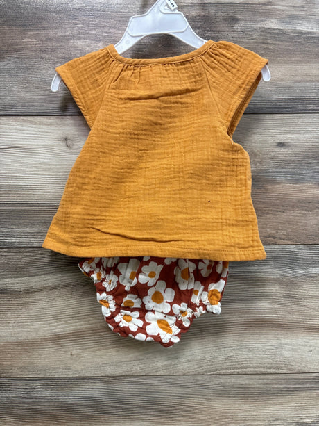 Front view of baby gauze top and daisy-print bloomers set, mustard orange top and rust floral bloomers on wood background