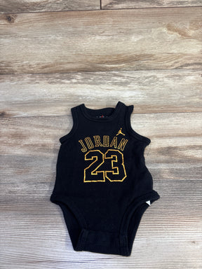 Flat lay of black infant Jordan tank bodysuit 6M showing gold JORDAN text, number 23, and Jumpman logo on wood background