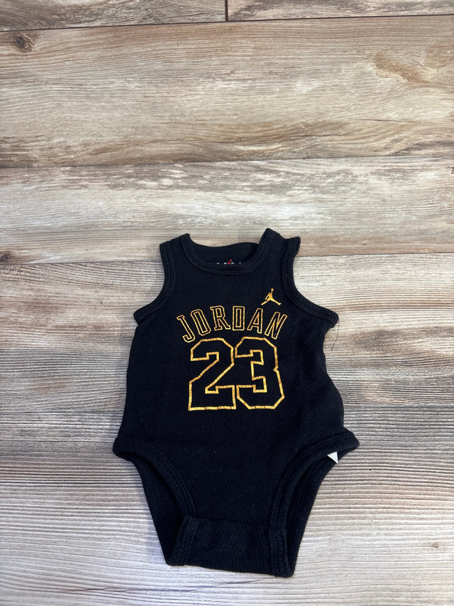 Flat lay of black infant Jordan tank bodysuit 6M showing gold JORDAN text, number 23, and Jumpman logo on wood background