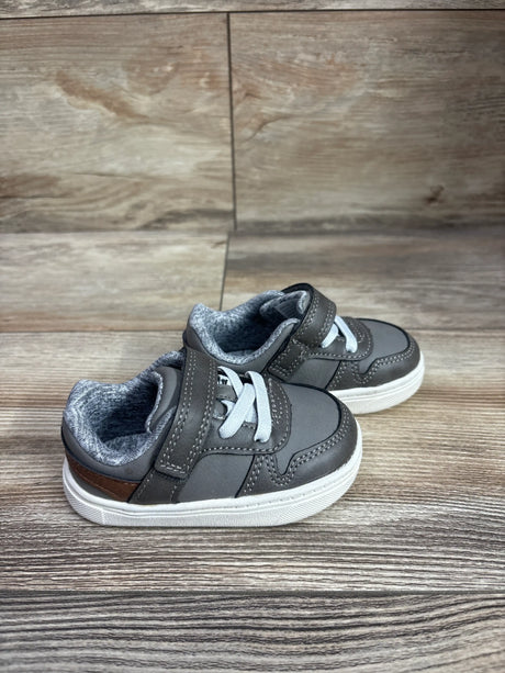 Angled view of Just One You First Walker sneakers showcasing gray uppers, white laces, hook-and-loop straps, and white soles