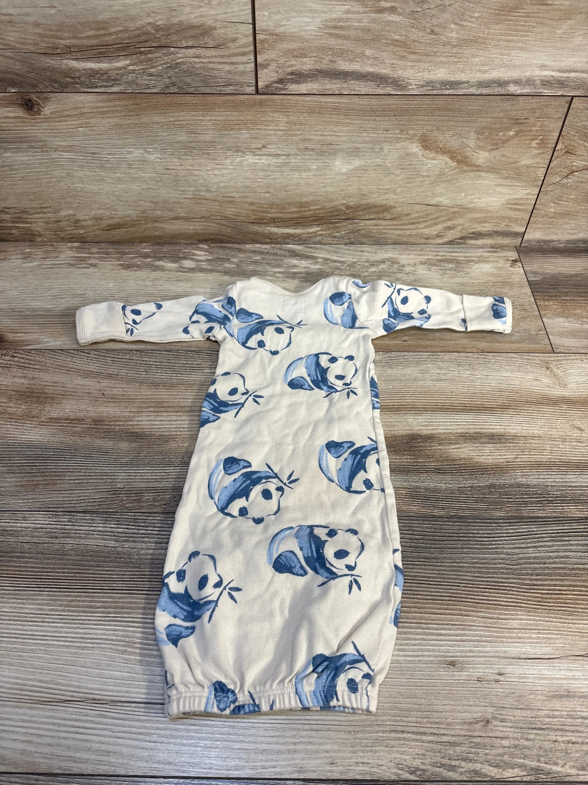 Flat-lay of newborn sleeper gown with blue panda print, long sleeves and elastic bottom opening on wood floor