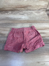 Flat lay of newborn red baby shorts showcasing elastic waistband, back pockets, and rolled hems on wood background