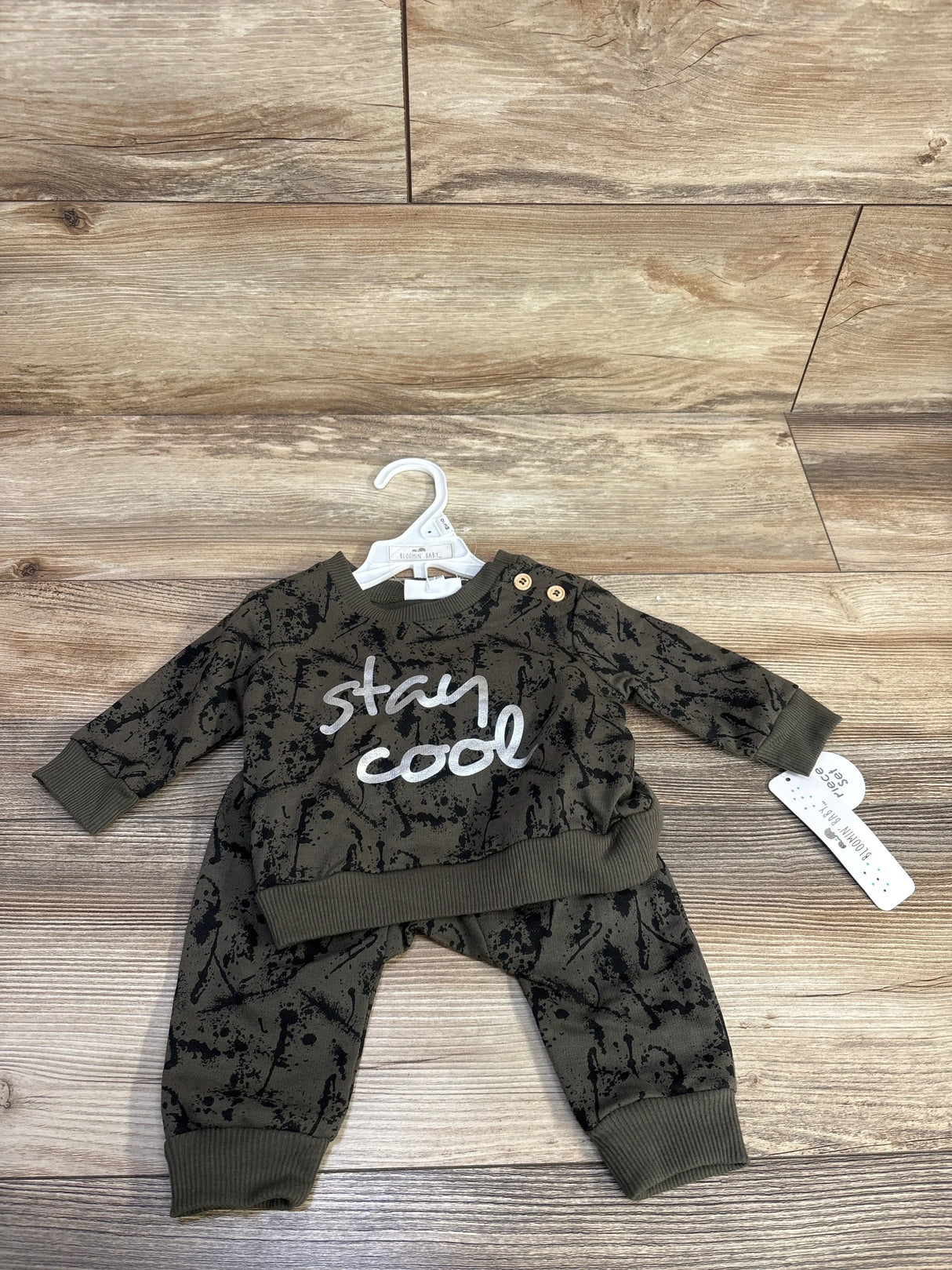 Front flat lay of newborn green sweatshirt and jogger set showing stay cool text and black splatter print on wood