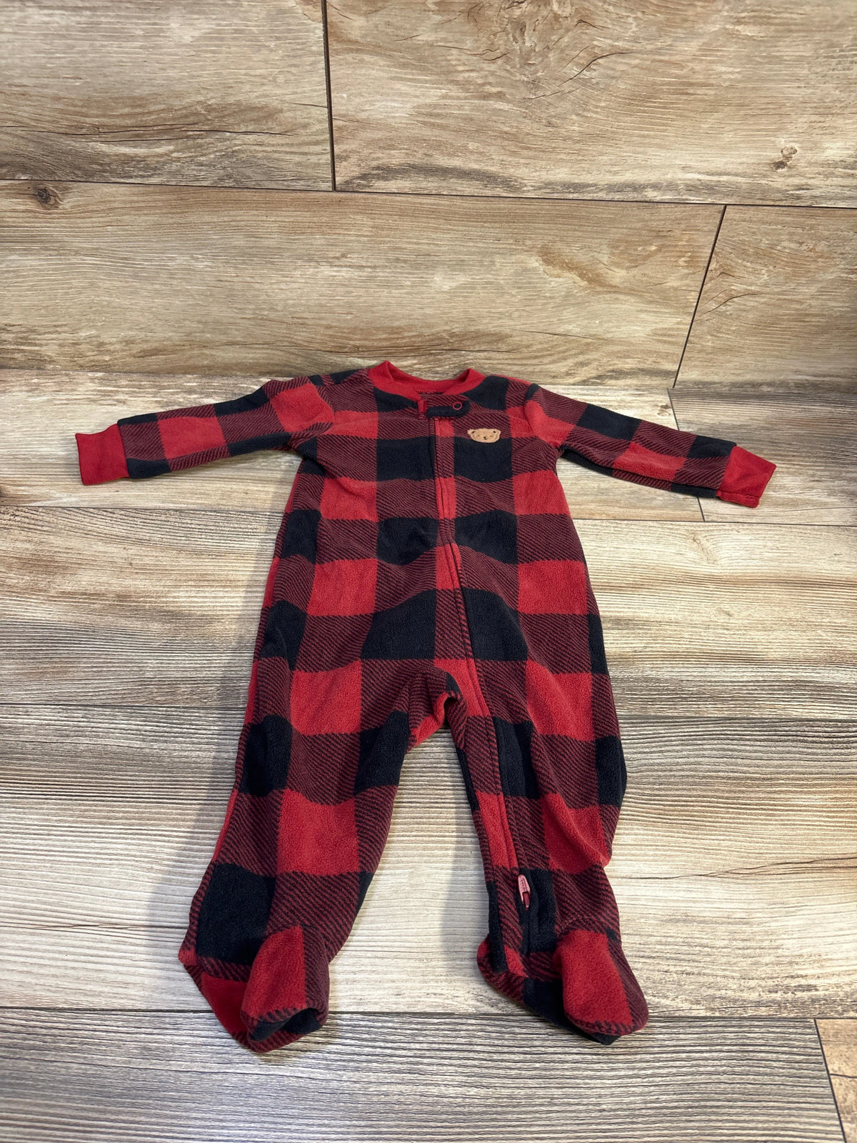 Top view of Child Of Mine blanket sleeper showcasing a red and black plaid pattern, front zipper, and enclosed feet on wood flooring