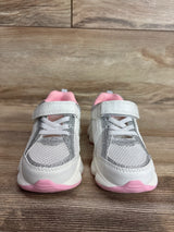 Front view of Carter's toddler white sneakers with silver glitter trim, pink lining and pink soles on wood floor