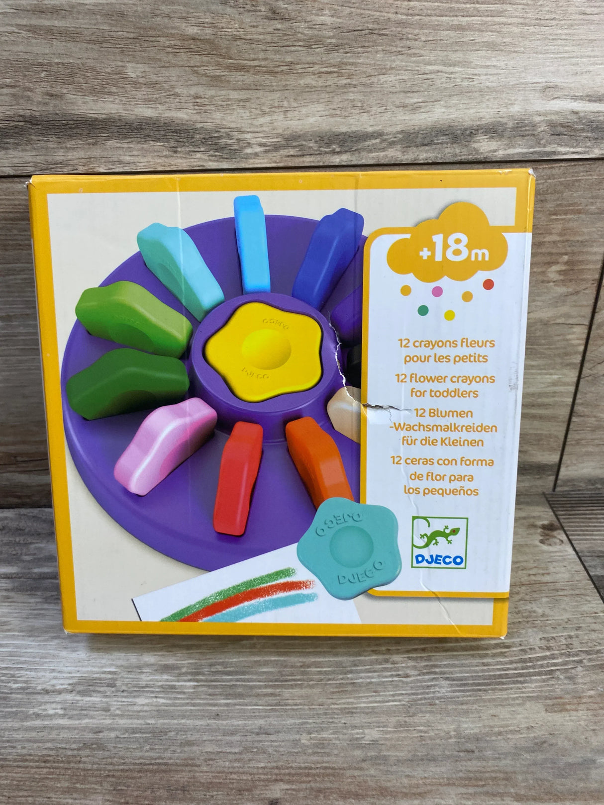 Front of Djeco Flower Crayons 12-pack box with purple flower holder, 12 chunky crayons and +18m label on wood