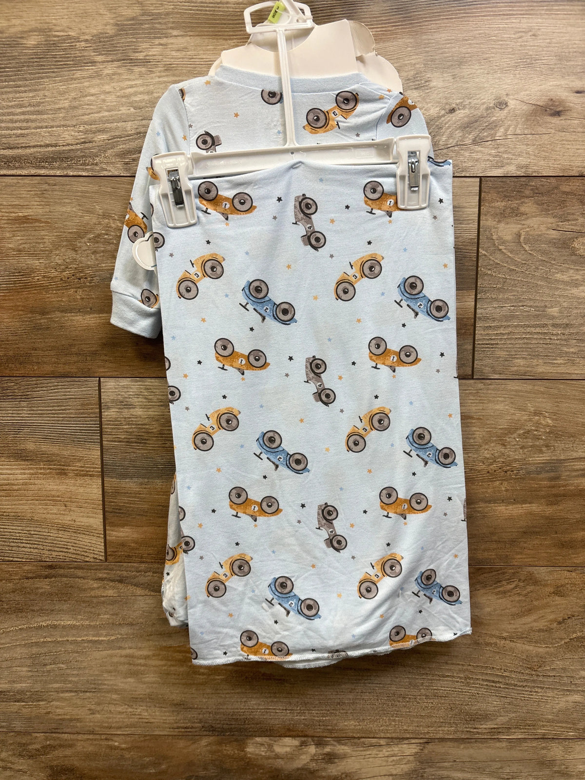 Front view of blue baby layette garment with colorful vehicle print on a wooden background