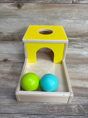 Wooden children's ball drop toy with yellow ramp and green and blue balls on wooden floor