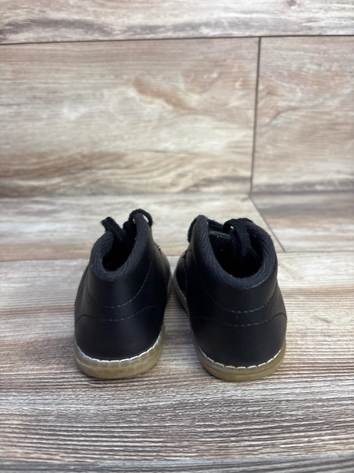 Rear view of Teeny Toes Oxford first walker baby shoes in black showing stitched gum sole and pull tabs on wood floor