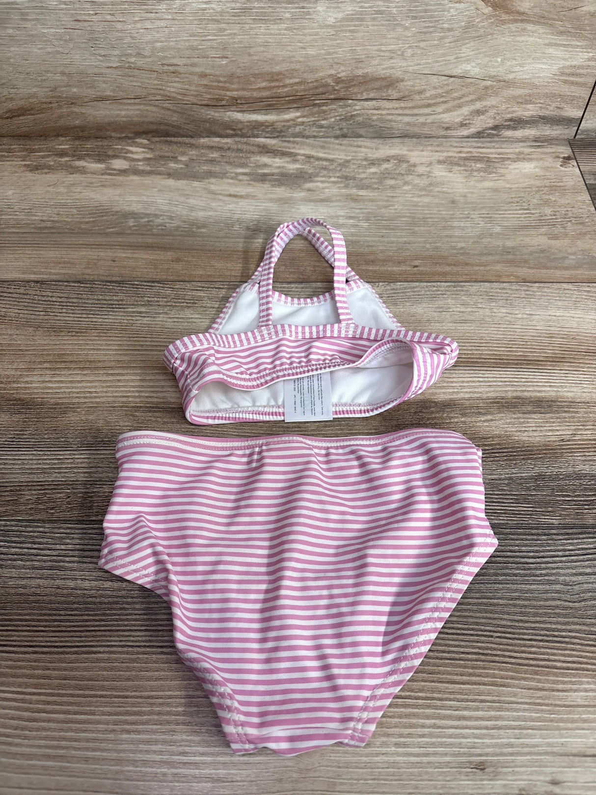 Top-down view of Carter's two-piece pink and white striped baby swimsuit showing halter-style top and high-waist bottoms on wood background