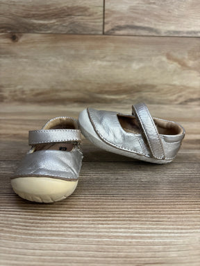 Pair of metallic silver toddler Mary Jane shoes with soft beige soles on wood surface
