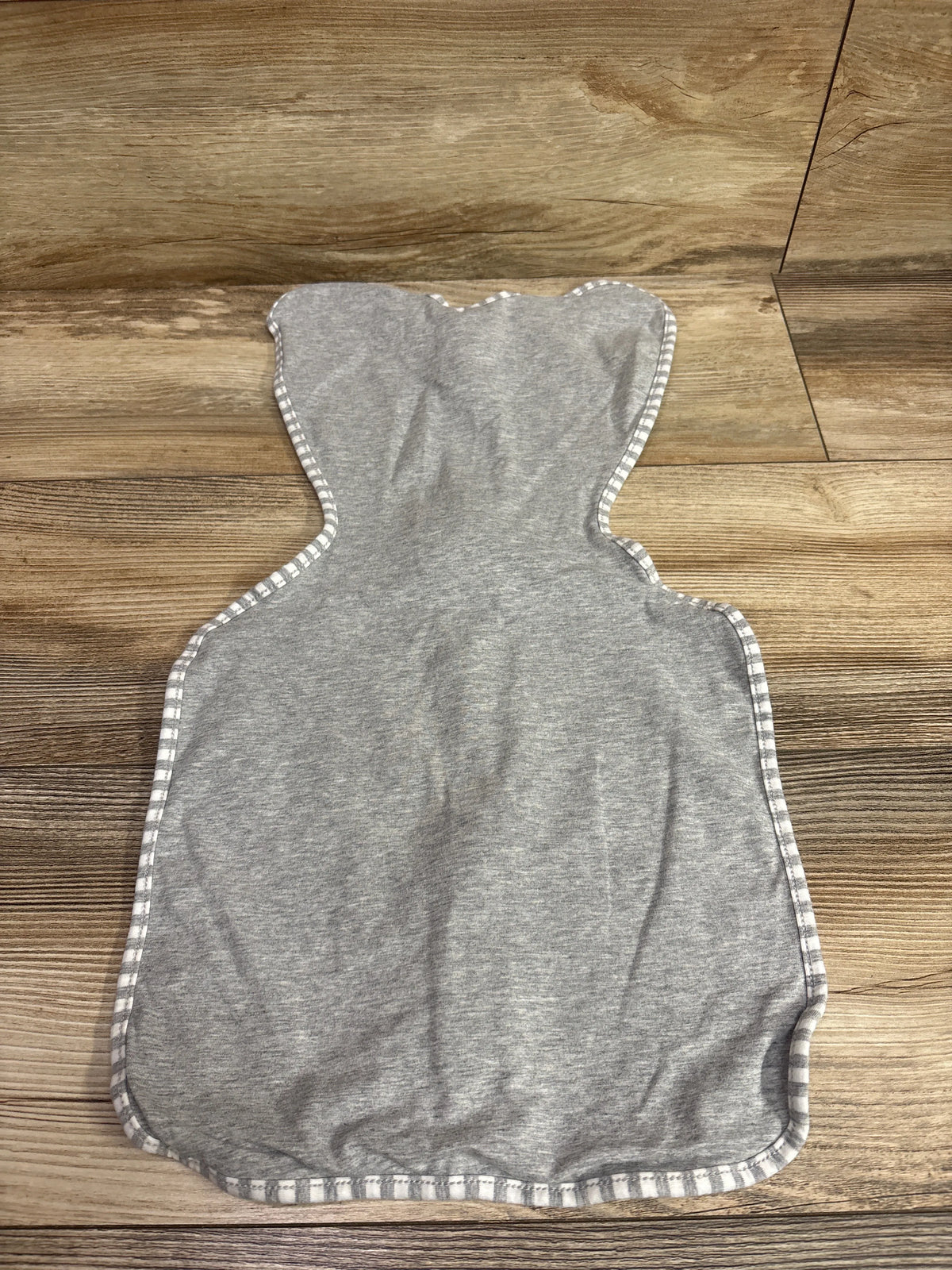 Flat view of Love To Dream Swaddle Up Original in gray, size Small/Newborn, showcasing striped trim on a wood-look floor