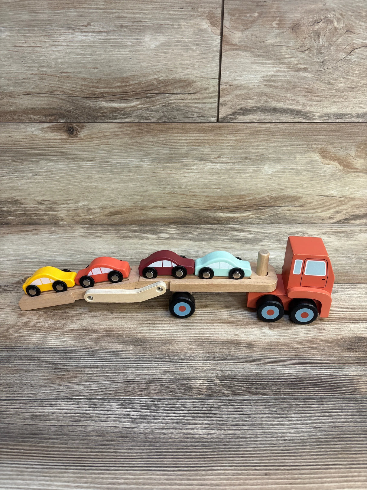 Wooden toy car carrier truck with four colorful cars on wood background