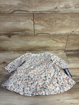 Flat lay of OshKosh smocked long-sleeve floral baby dress showing smocked bodice, ruffle hem and brand tag on wood background