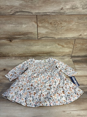 Flat lay of OshKosh smocked long-sleeve floral baby dress showing smocked bodice, ruffle hem and brand tag on wood background