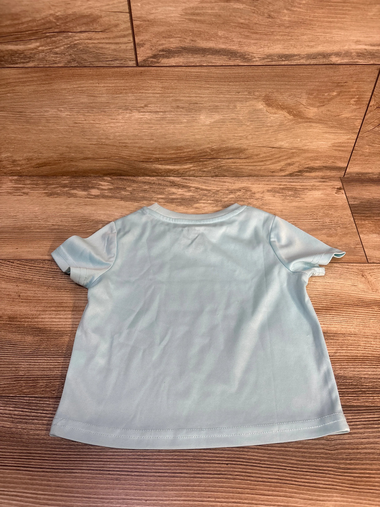 Light blue toddler t-shirt laid flat on wood floor, kids clothing resale