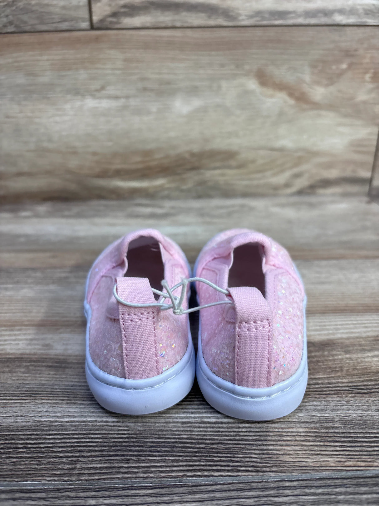 Rear view of pink Cat and Jack toddler glitter slip-on sneakers with elastic bungee tie and white rubber soles on wood
